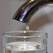 Tap dripping into a filled water glass