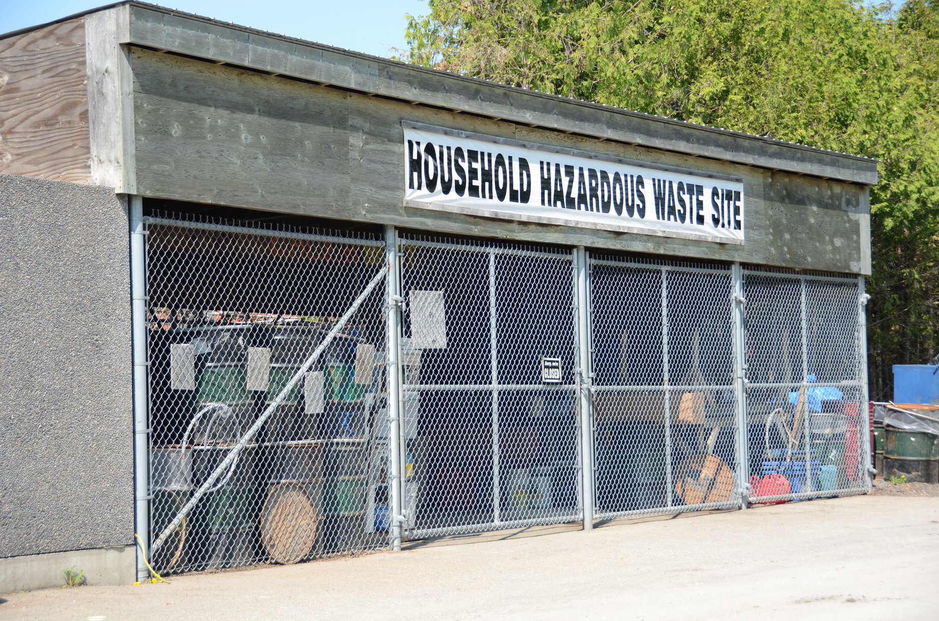 Picture of cement structure with chain link fencing and a sign reading 'Household Hazardous Waste'