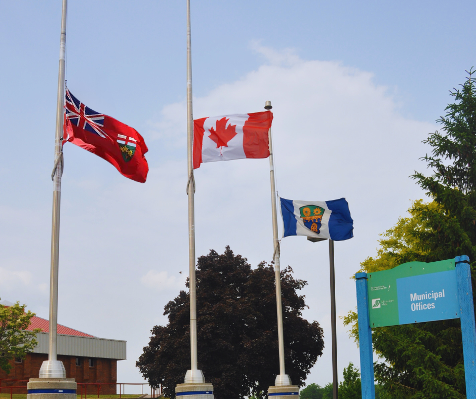 Photo of three flags at half mast with a blue and green sign to the right