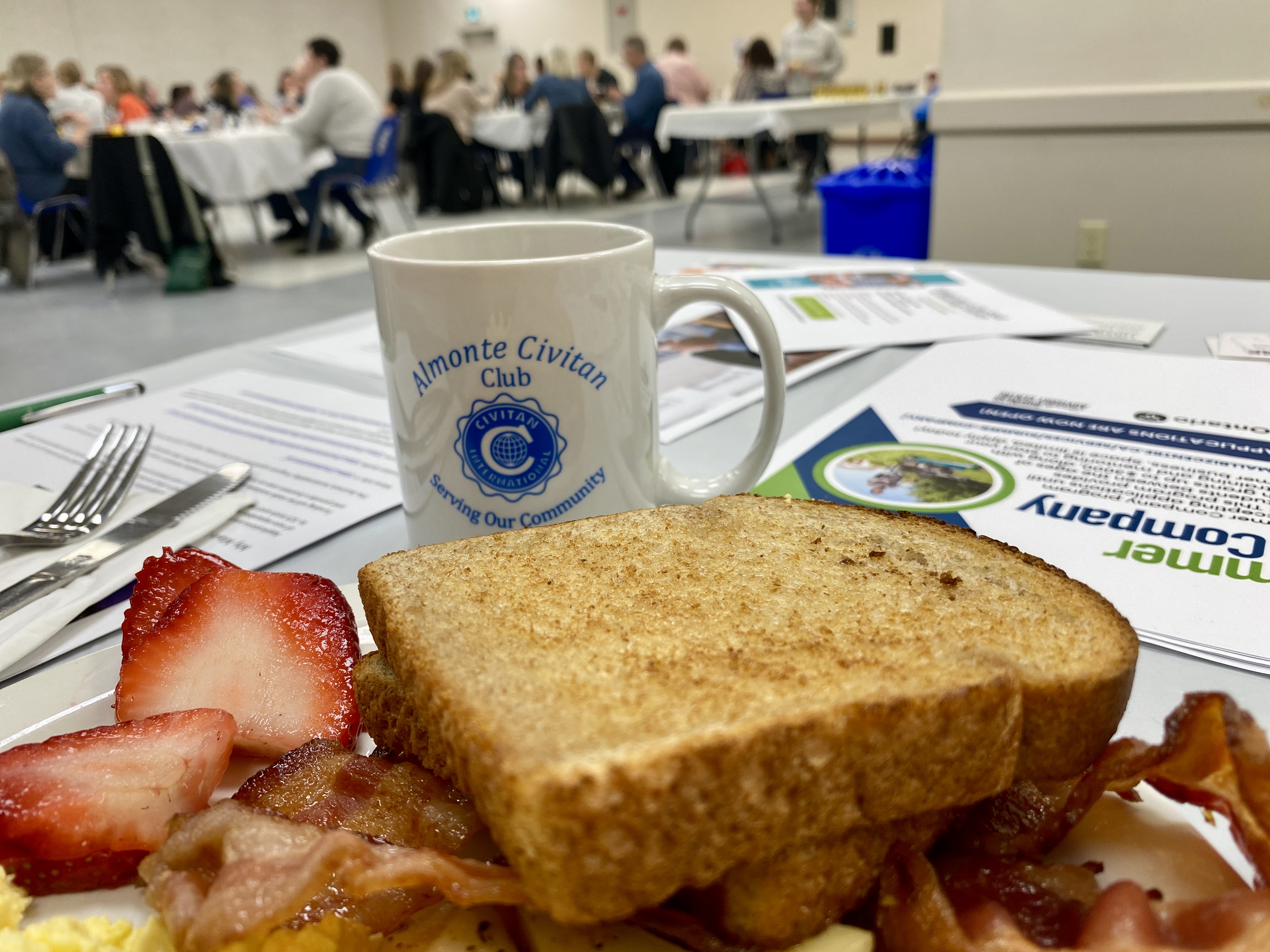 Close up of plate with toast, strawberries and bacon. White mug with blue lettering 'Almonte Civitan Club' sits in front.