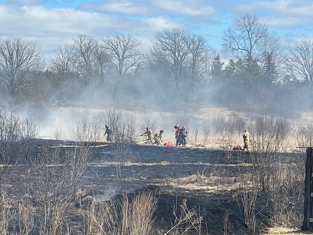 Photo of firefighters fighting grass fire with in a charred field