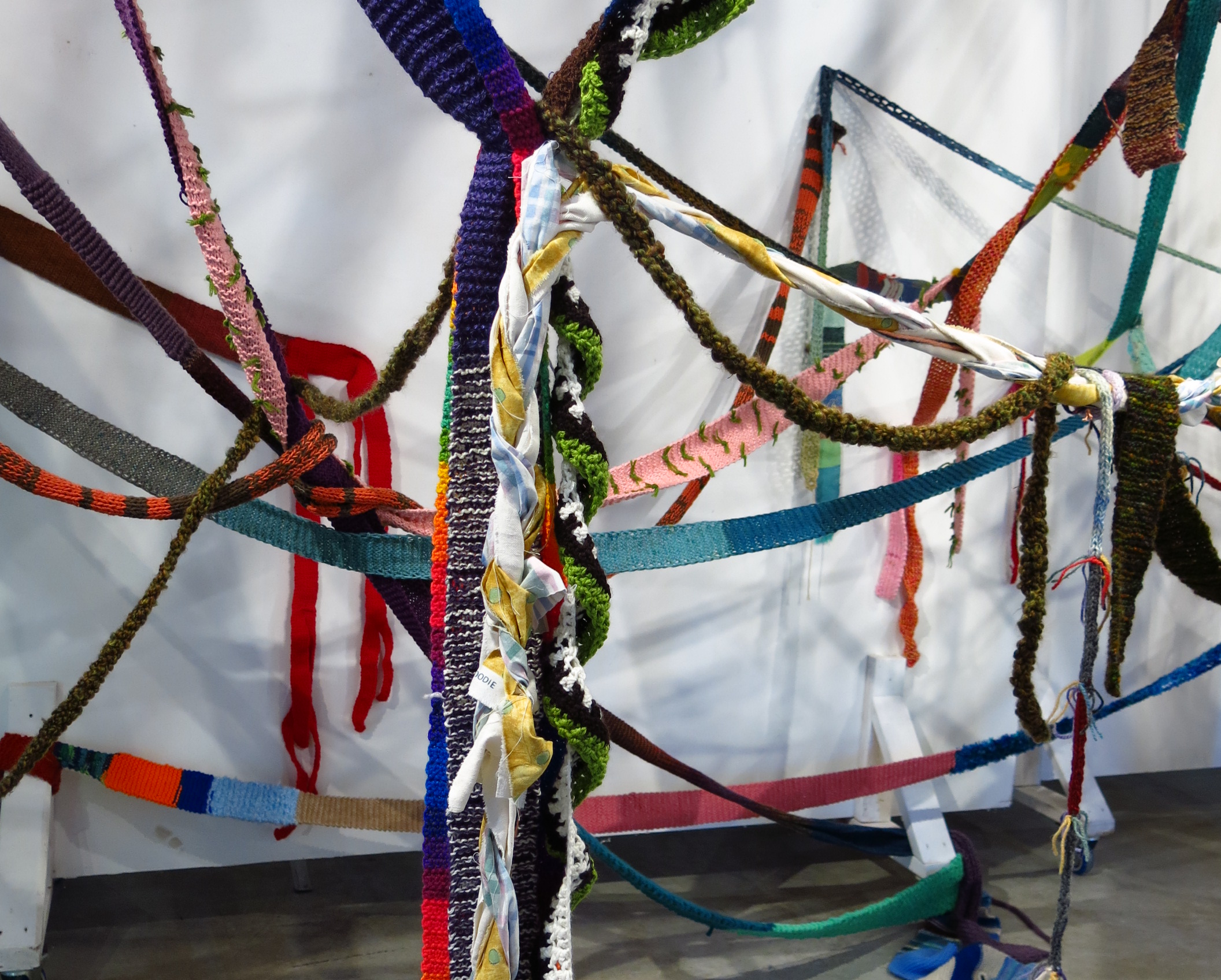 Brightly coloured textiles roped together hang from a ceiling