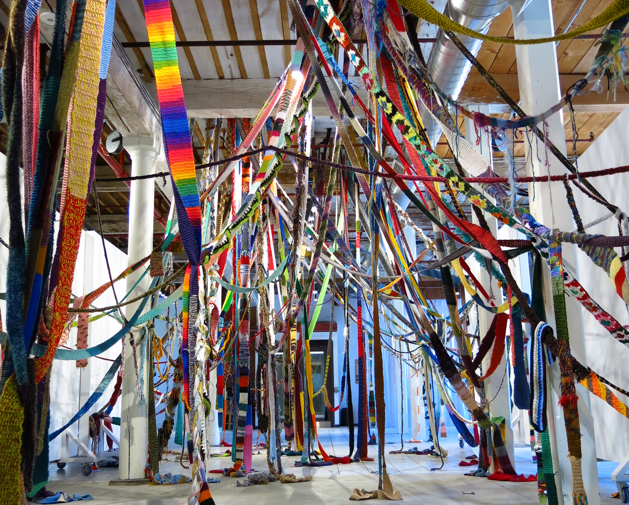 Ribbons of brightly coloured textiles hang from a ceiling in a museum
