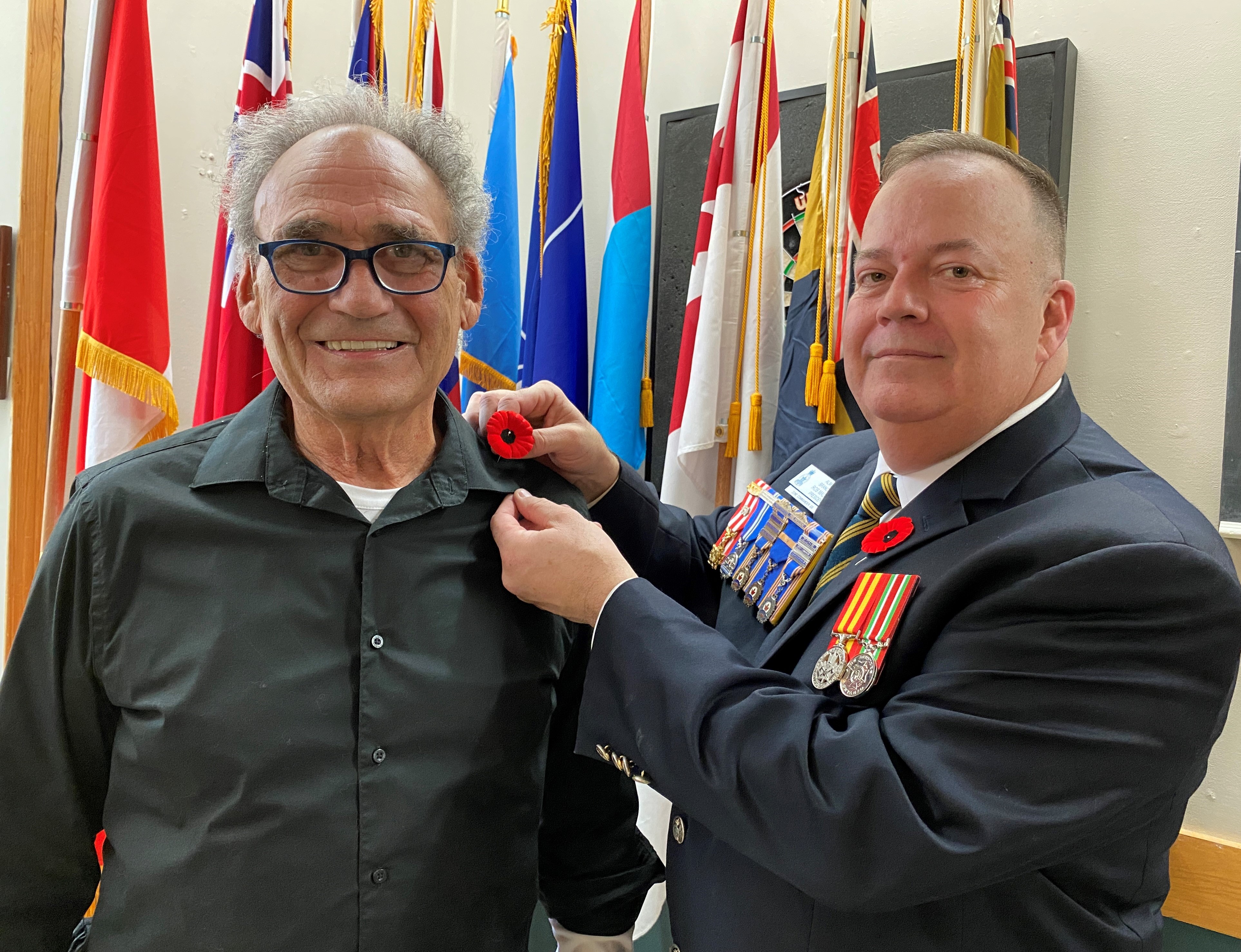 Two men standing in front of flags with one man pinning poppy to lapel