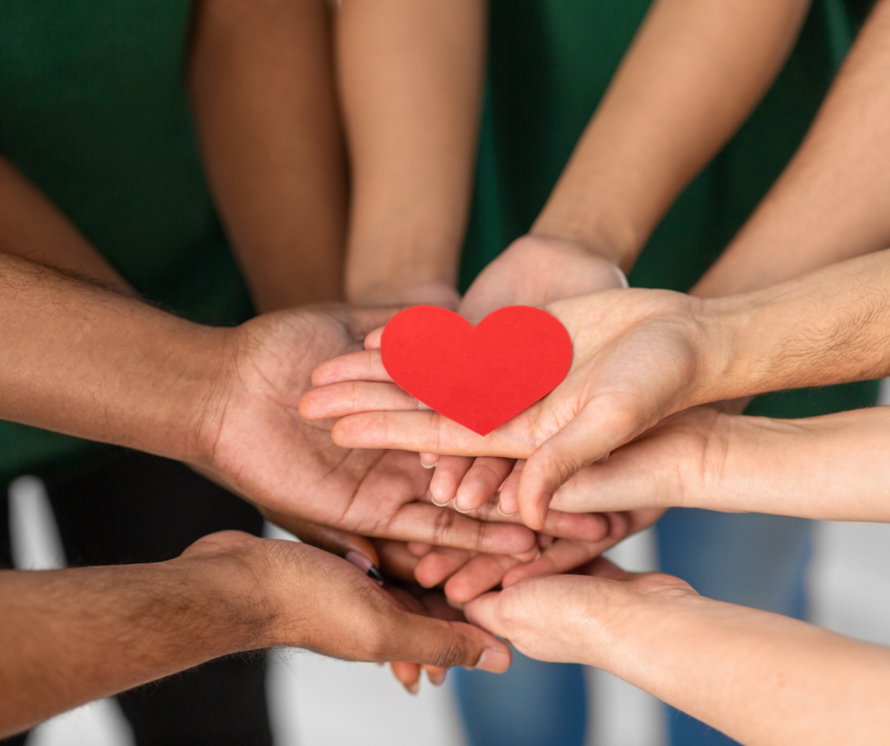 Group of people place their hands on top of each others with a red heart on top