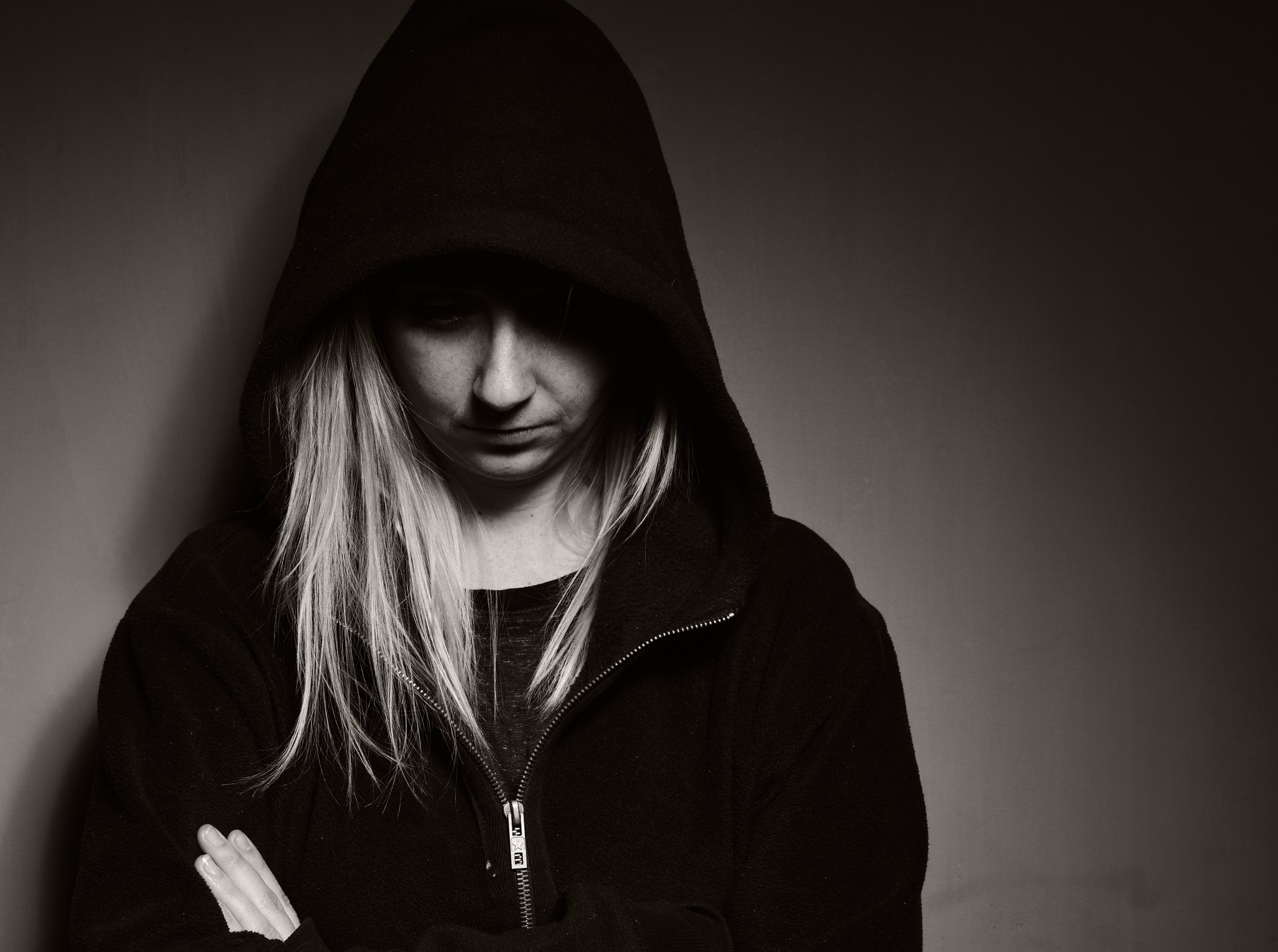 Black and white photo of a young woman looking down, wearing a black hoodie with hood covering portion of her face