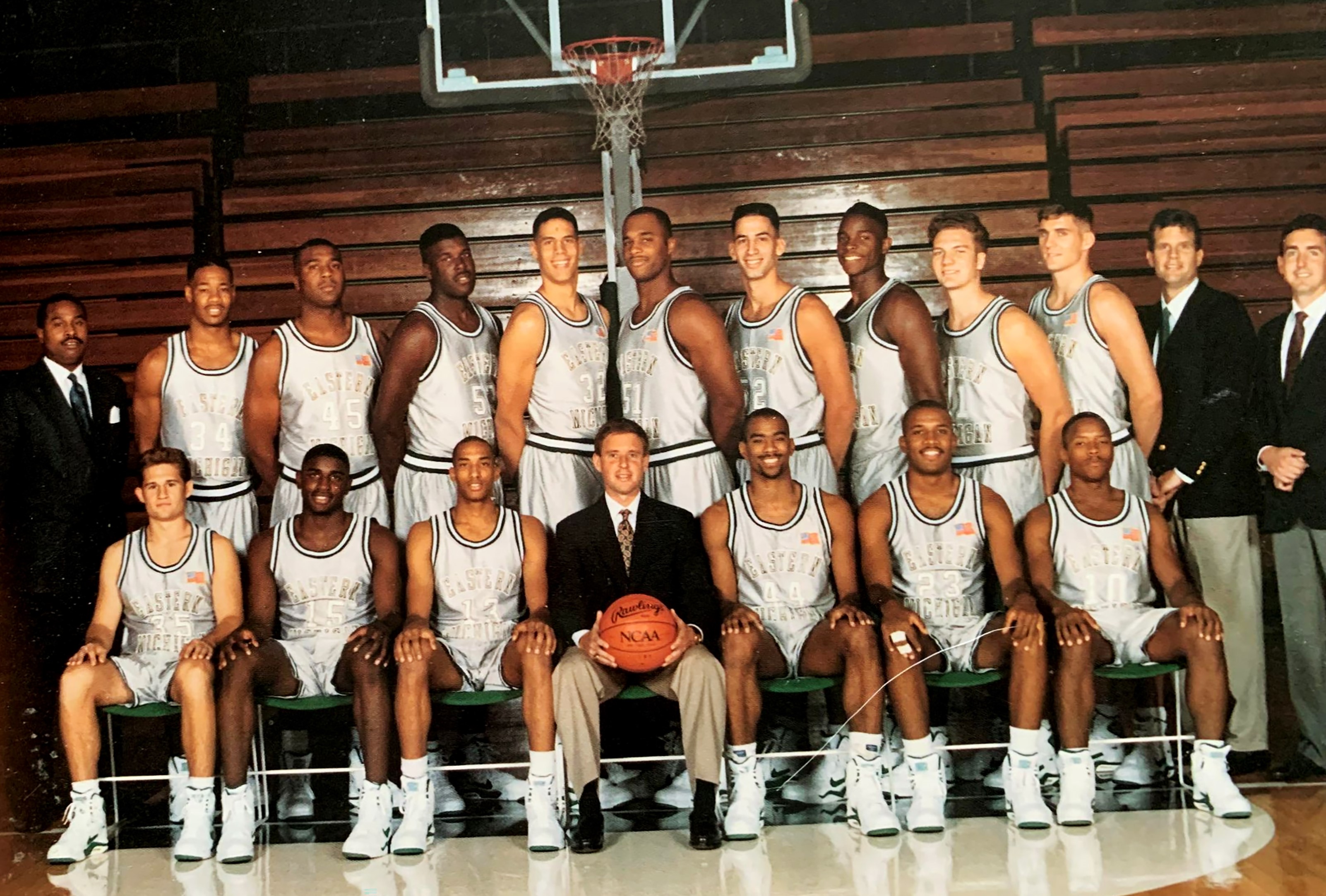 Basketball players stand and sit for a team photo in a gymnasium