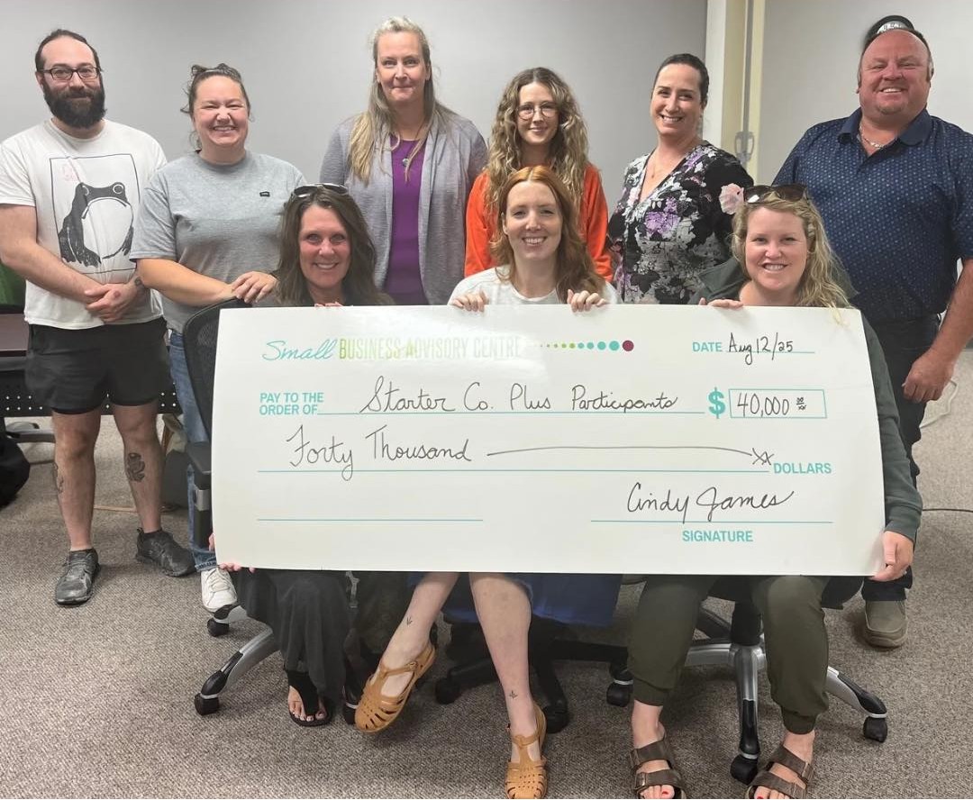 Two rows of people (back row standing, front row sitting) with a large cheque