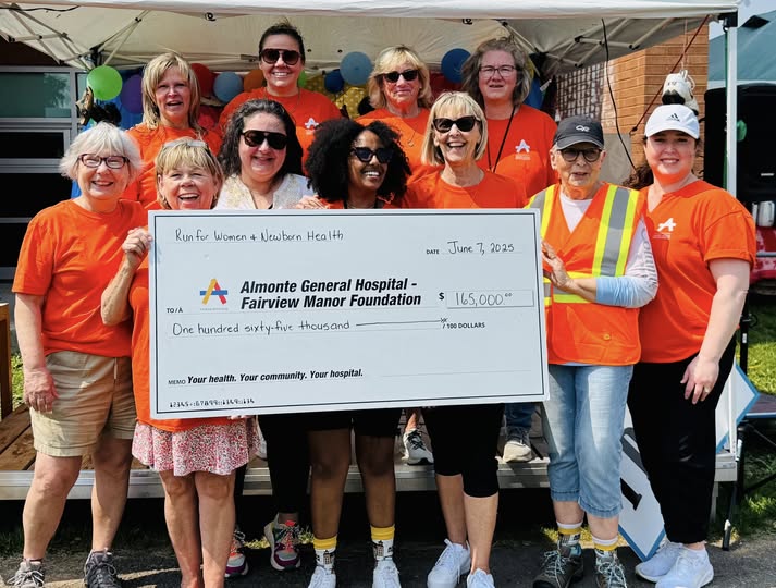 Photo of group of people in two rows, wearing bright orange shirts and holding a large white cheque
