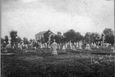 Black and white photo of cemetery in foreground with stone church in background