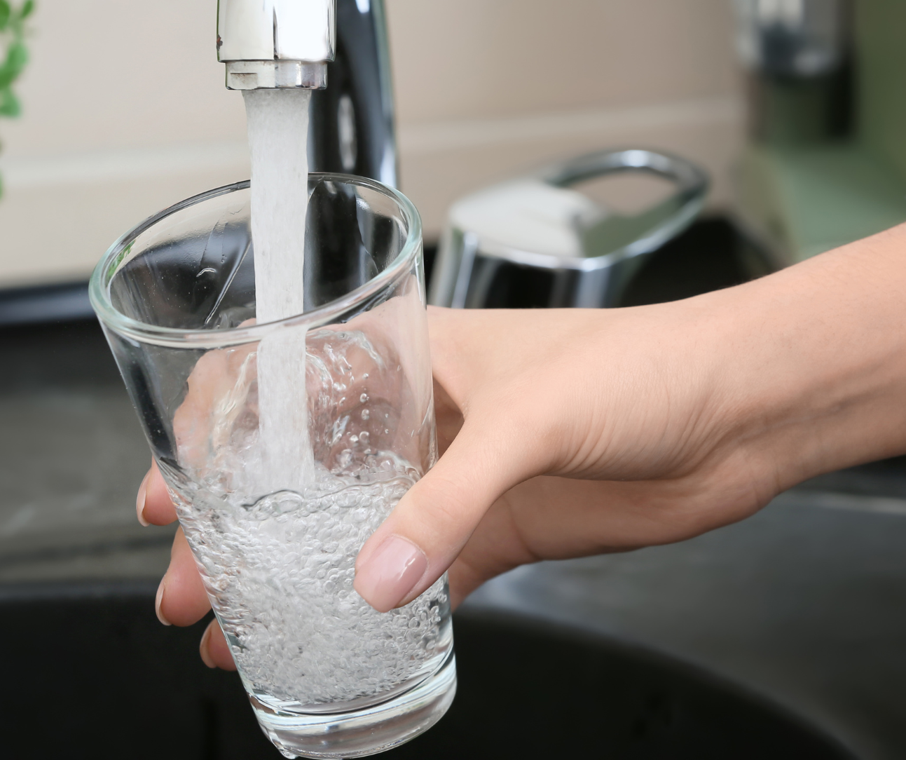 Photo of a person holding a clear glass under a kitchen faucet and filling it with water