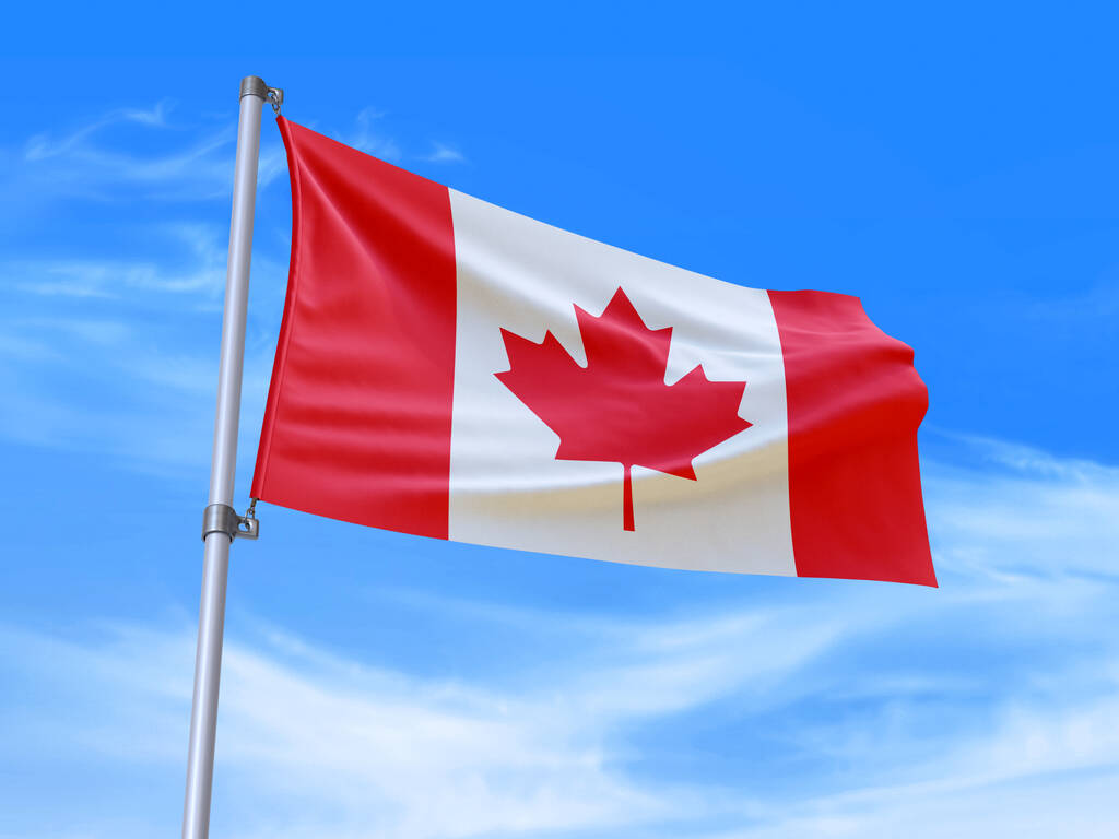 Photo of red and white Canadian flag with red maple leaf in the centre flying on a flagpole against a blue sky