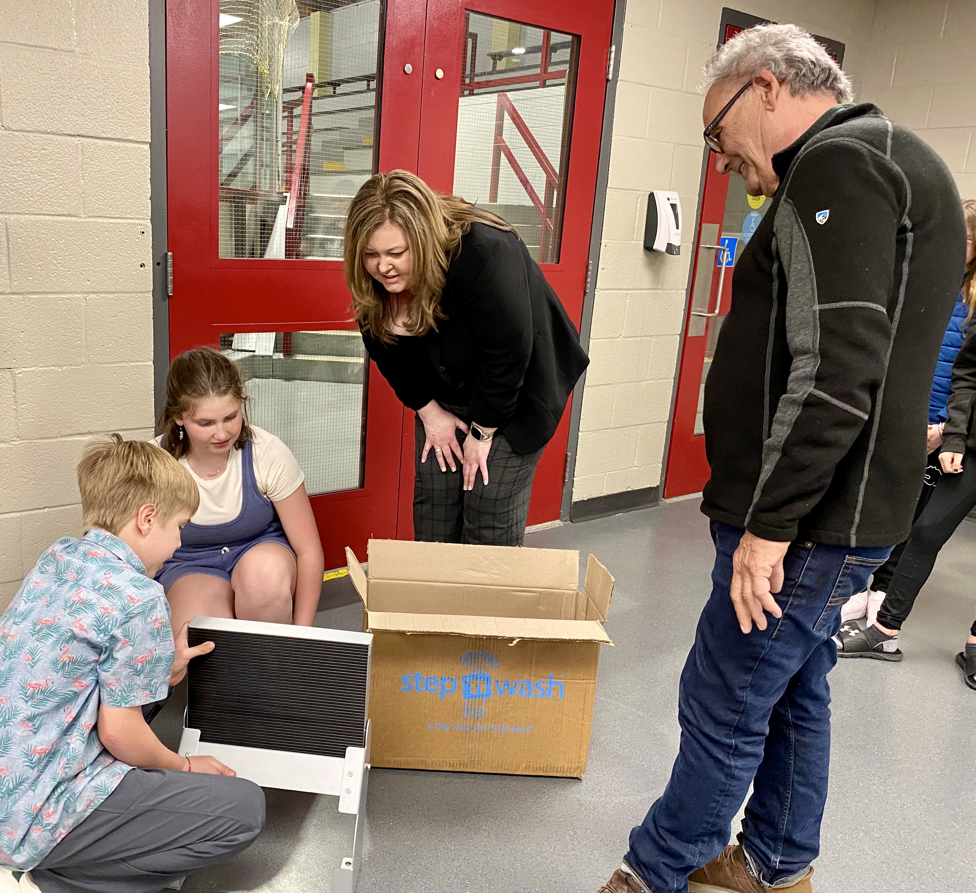 Two students crouch down, showing two adults a piece of equipment