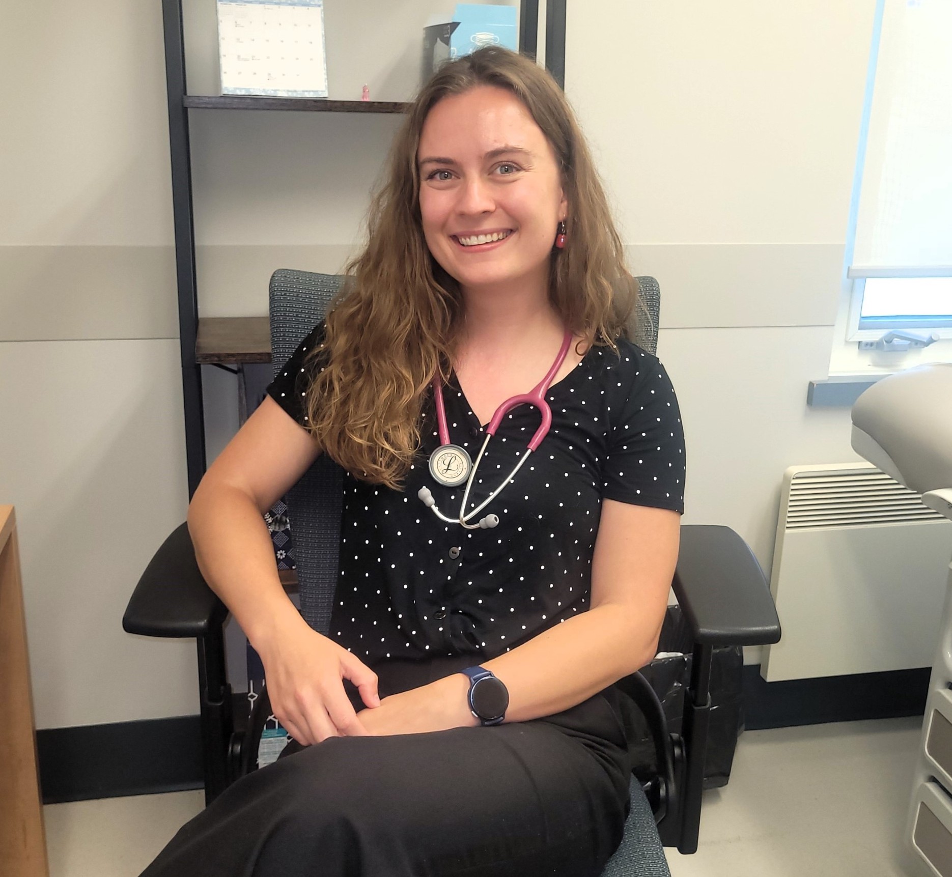 Woman with brown hair sits in a clinic room with stethoscope around her neck