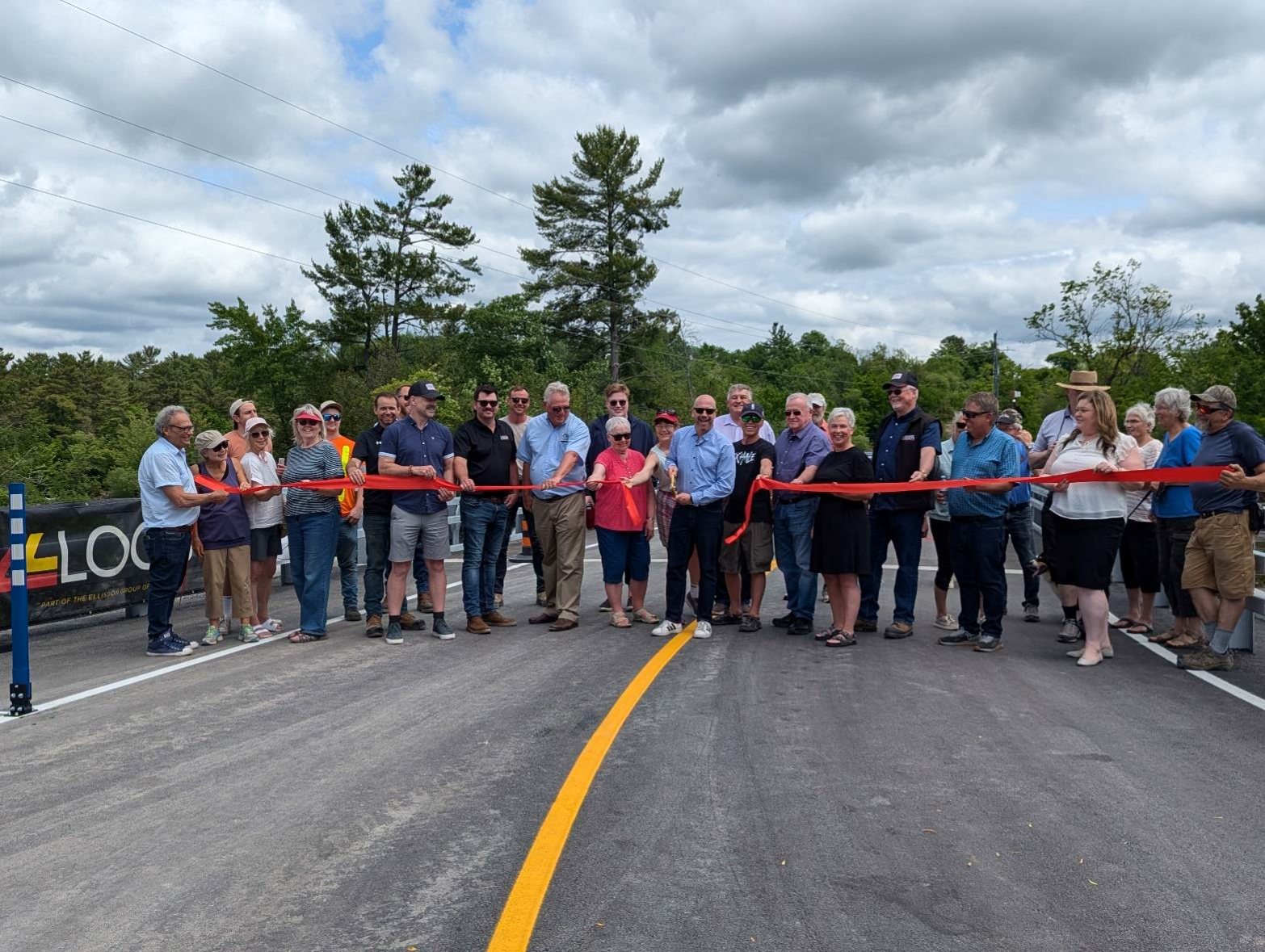 A large group of people stand on a bridge holding a red ribbon