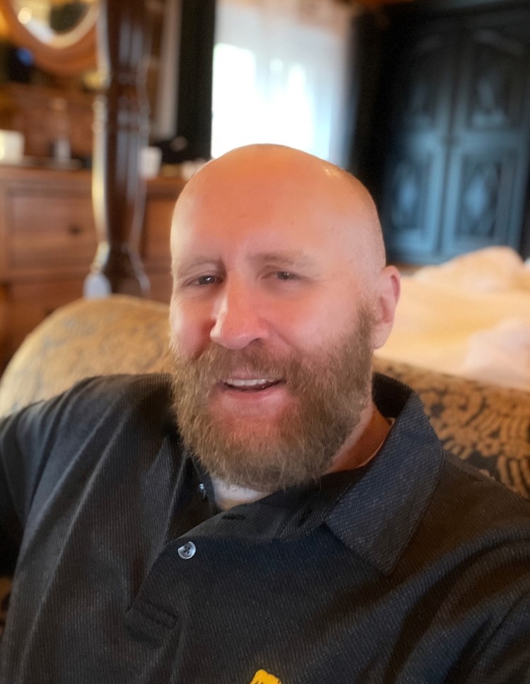 Headshot of bald man with facial hair sitting on a couch