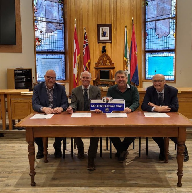 Photo of four men sitting at a wooden table in council chambers