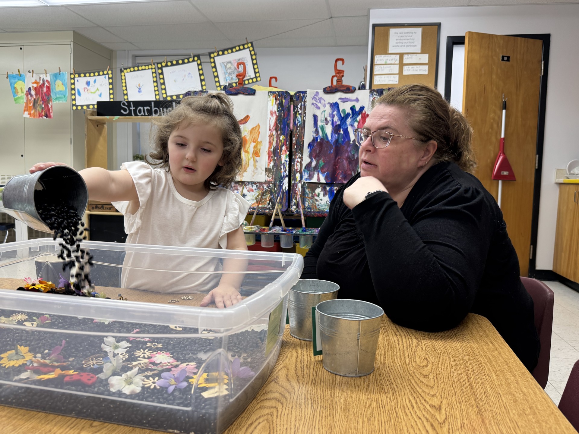 Woman supervises a child sitting at a table playing