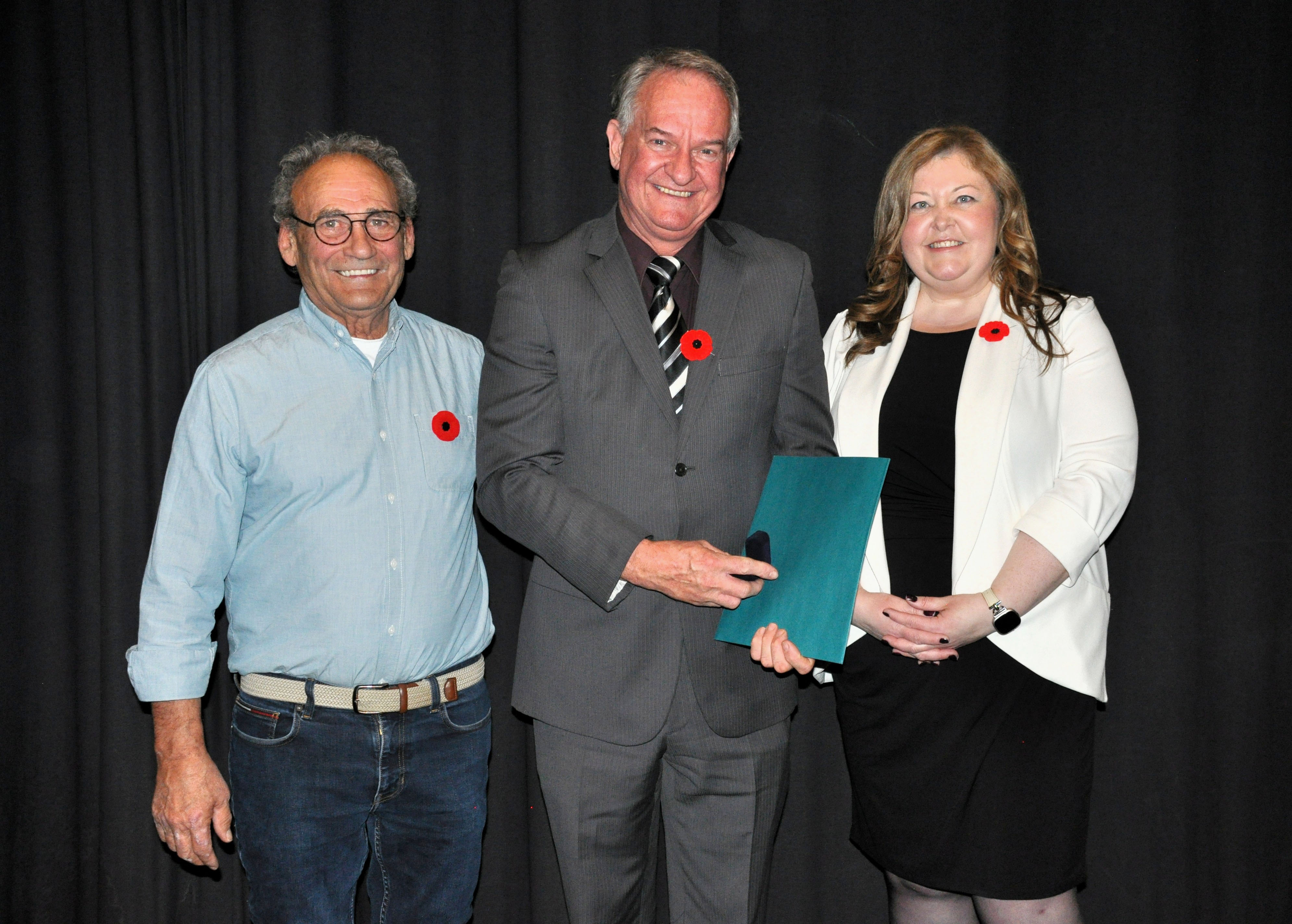 Three people pose for a photo against a black curtain