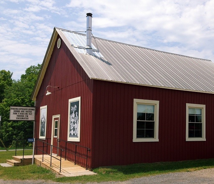 Photo of schoolhouse building with red siding and tin roof