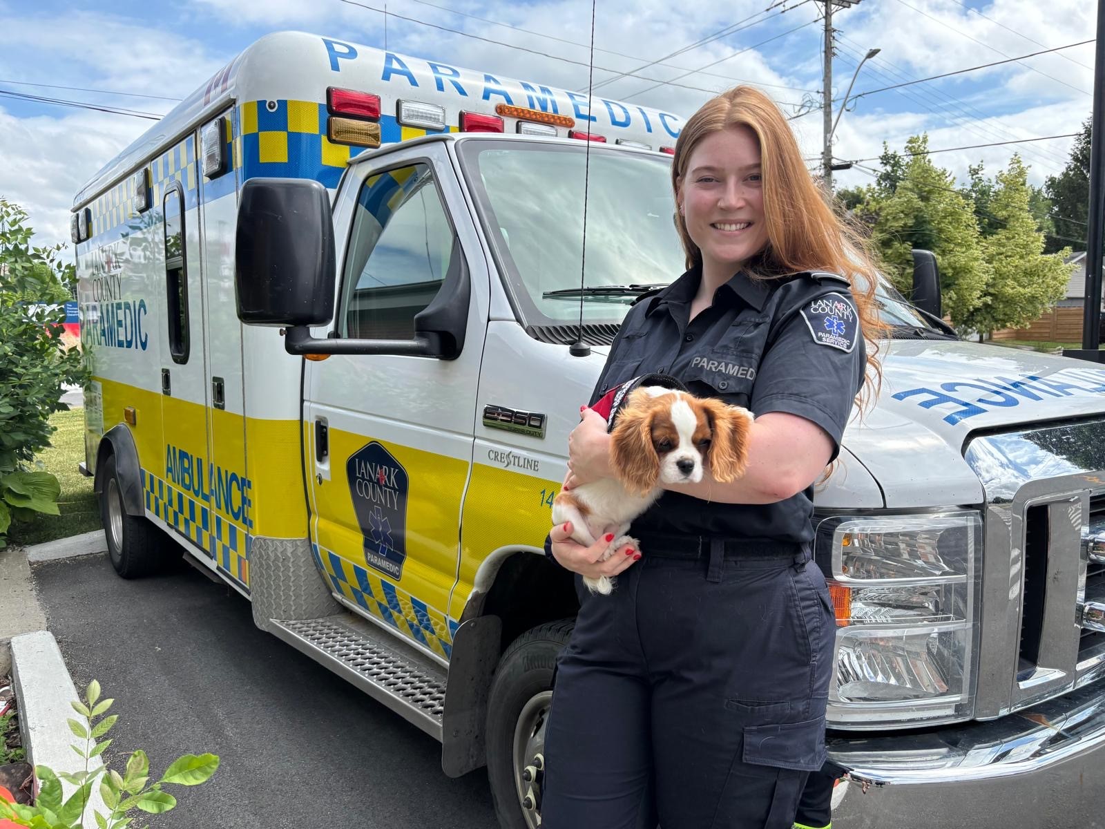 Lanark County paramedic stands in front of an ambulance holding a puppy