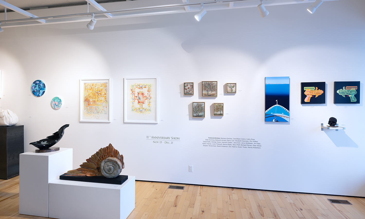 Photo of art gallery with colourful artwork adorning white wall and sculpture sitting on white blocks