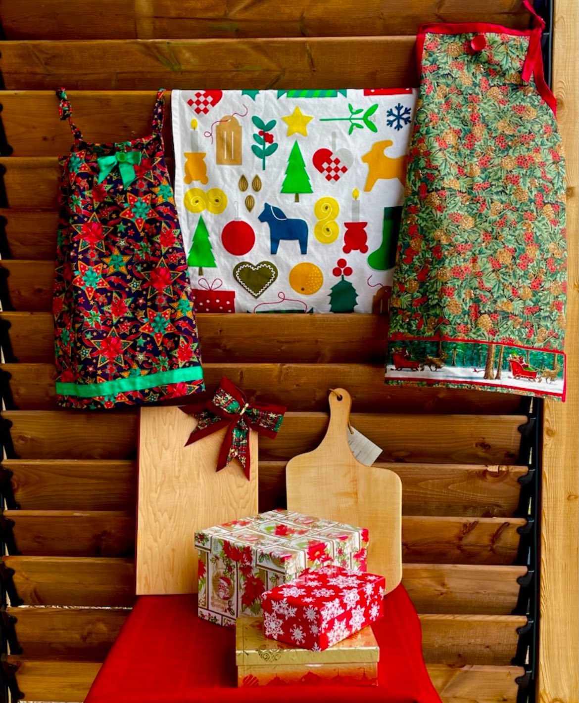 Photo of colourful Christmas aprons, cutting boards propped up against a wooden wall