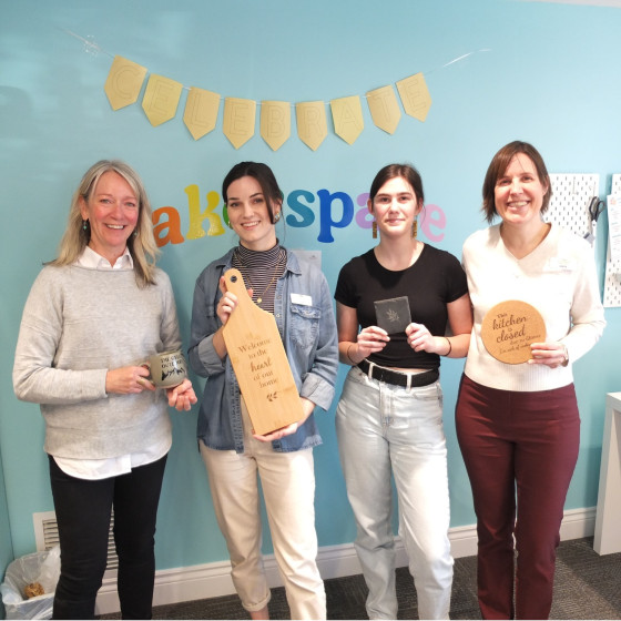 A group of women stand together against a light blue wall holding items