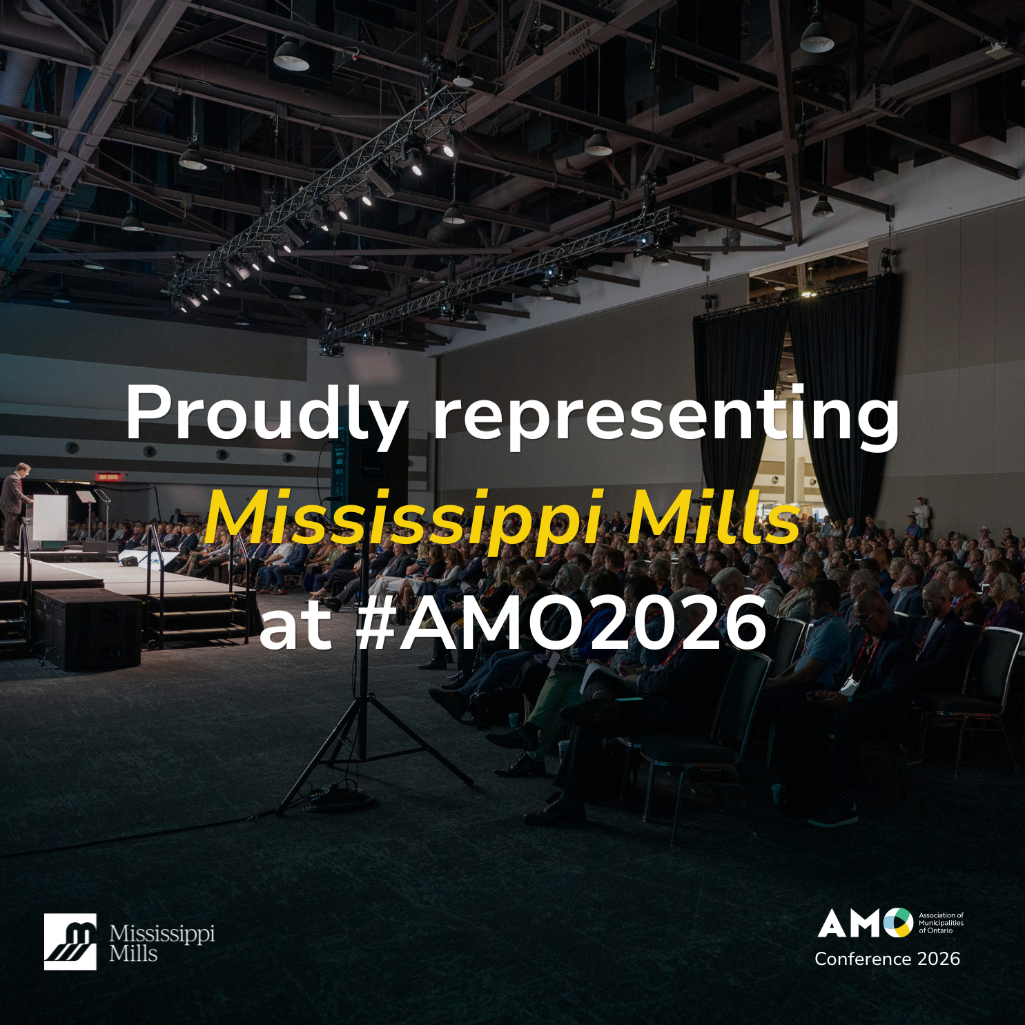 A conference room full of people listens to a speaker on a stage. White and yellow text reads 'Proudly representing Mississippi Mills at #AMO2026.'