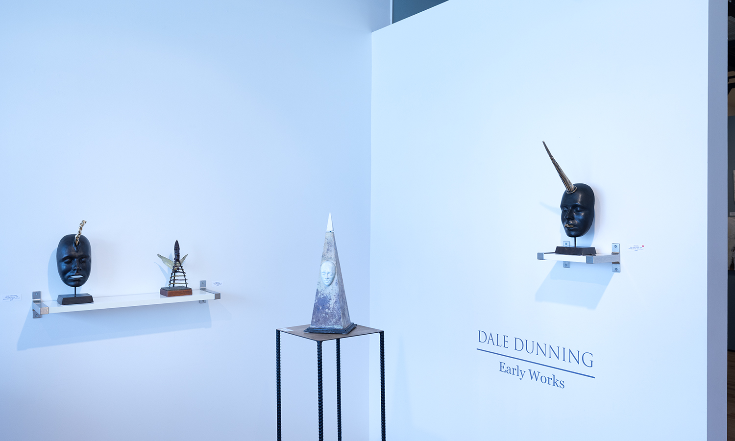 Photo of sculptures on shelves and a table against a white gallery wall