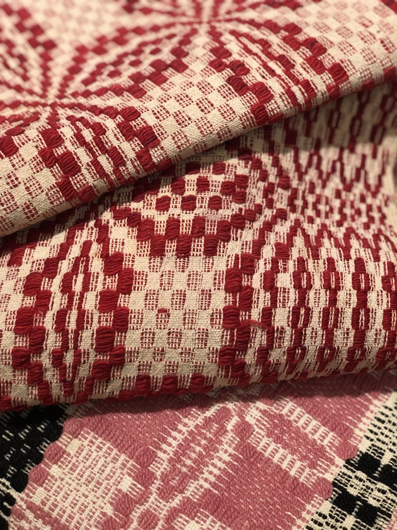 Up close photo of detailing on a red and cream coloured coverlet