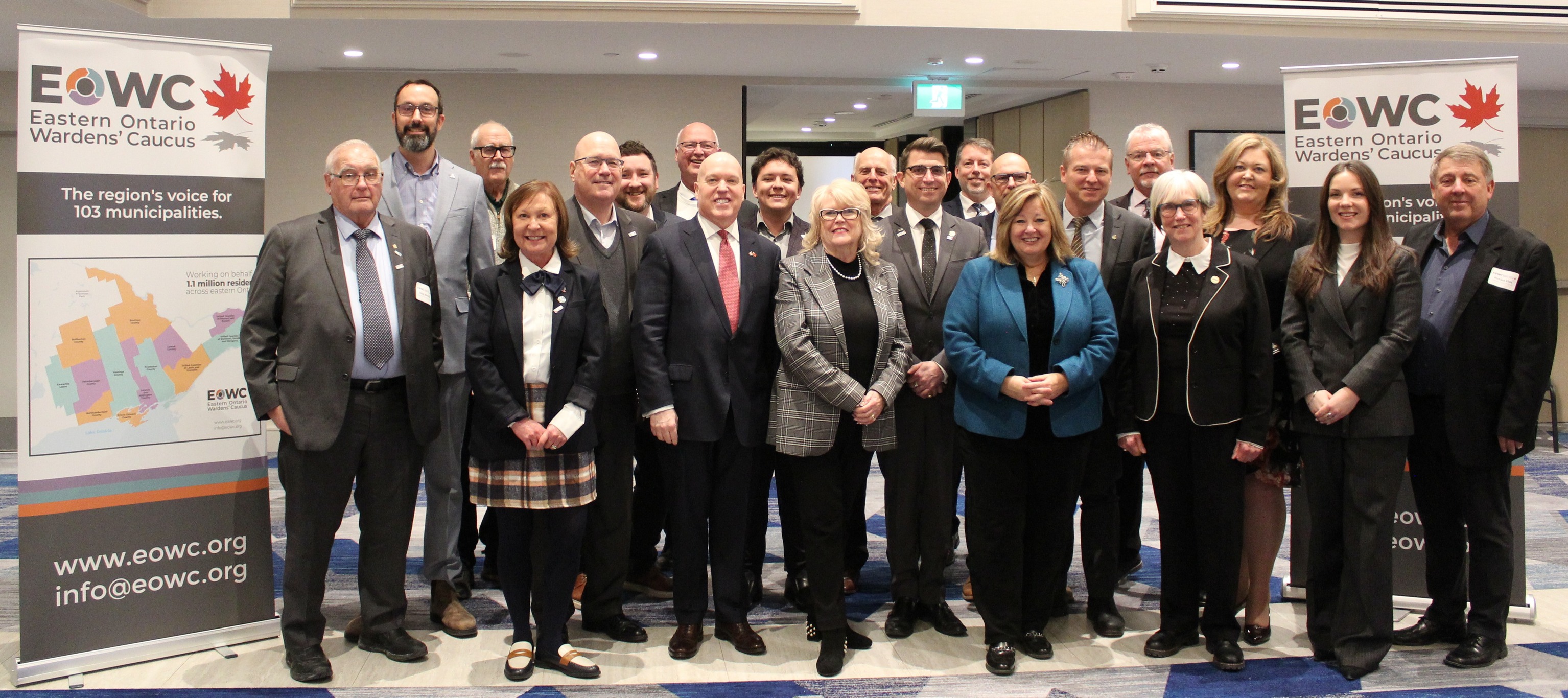 A large group of people stand in a room flanked by two large banners