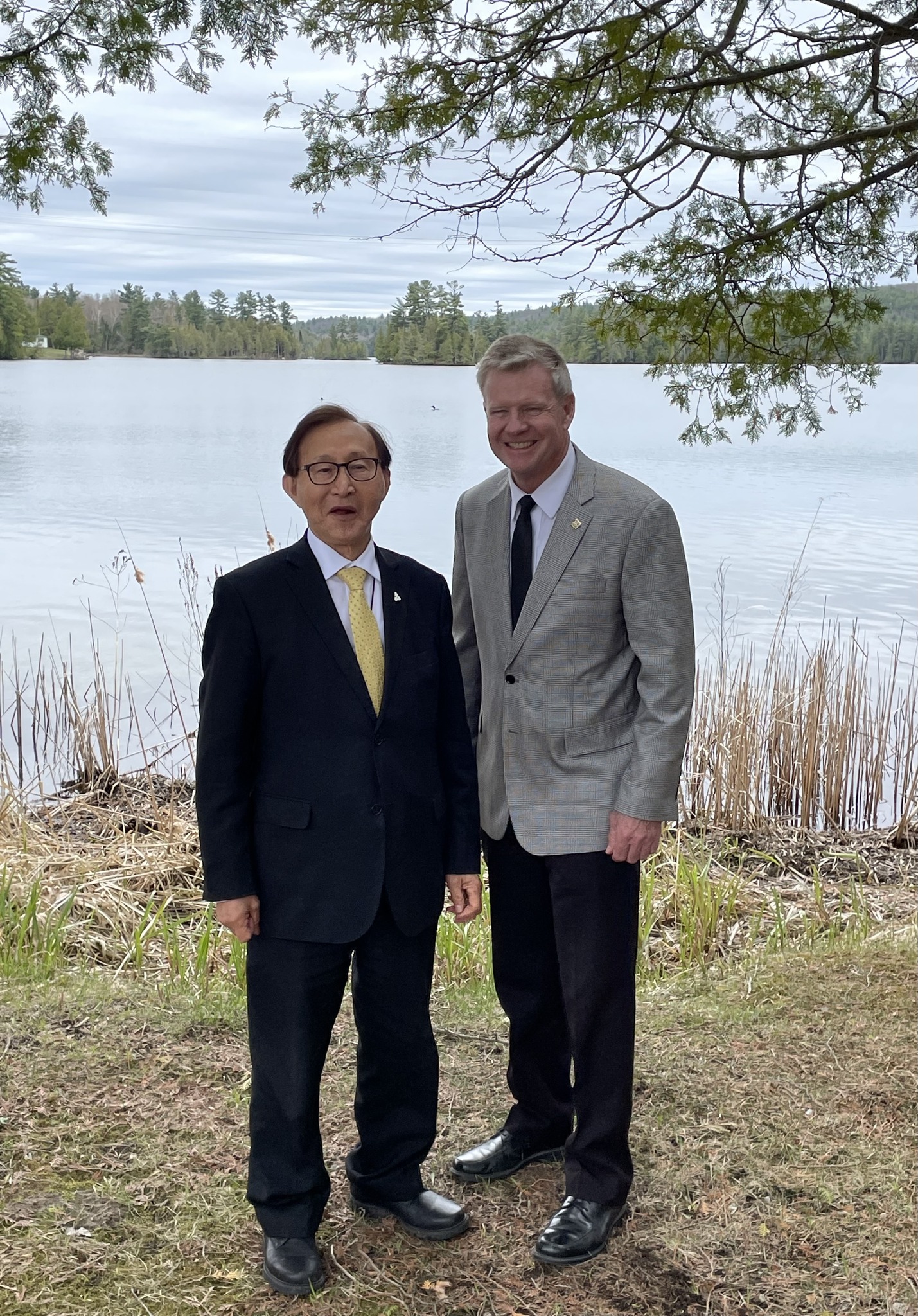 Two men pose for a photo by a lake