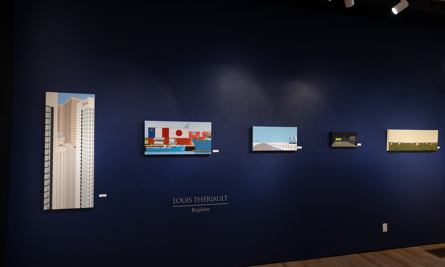 Artwork hangs in a gallery against a dark blue wall