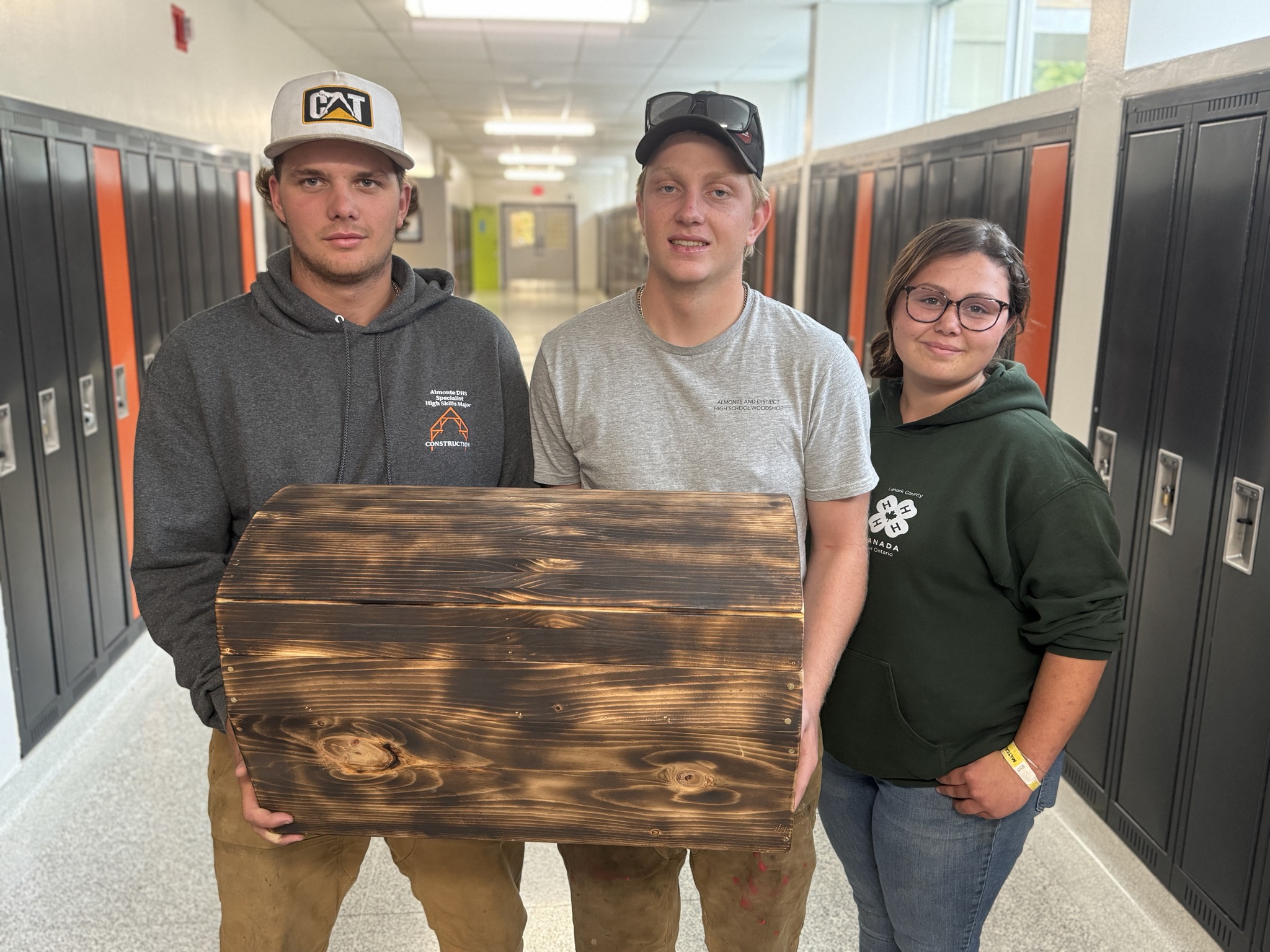 Three students hold a wooden chest in the hallway of a school