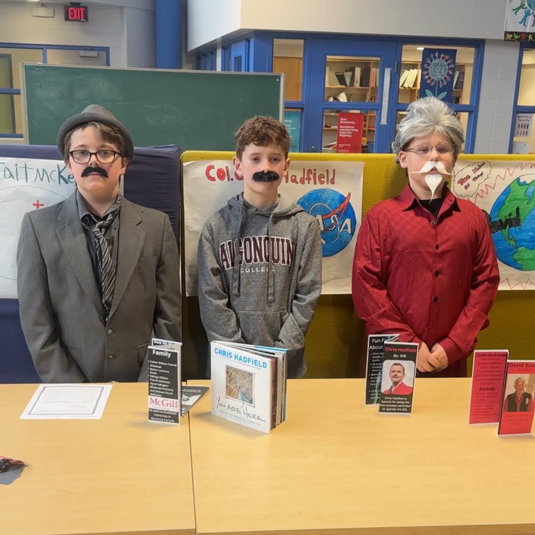 Three students dressed in costume with moustaches pose for a photo in a school