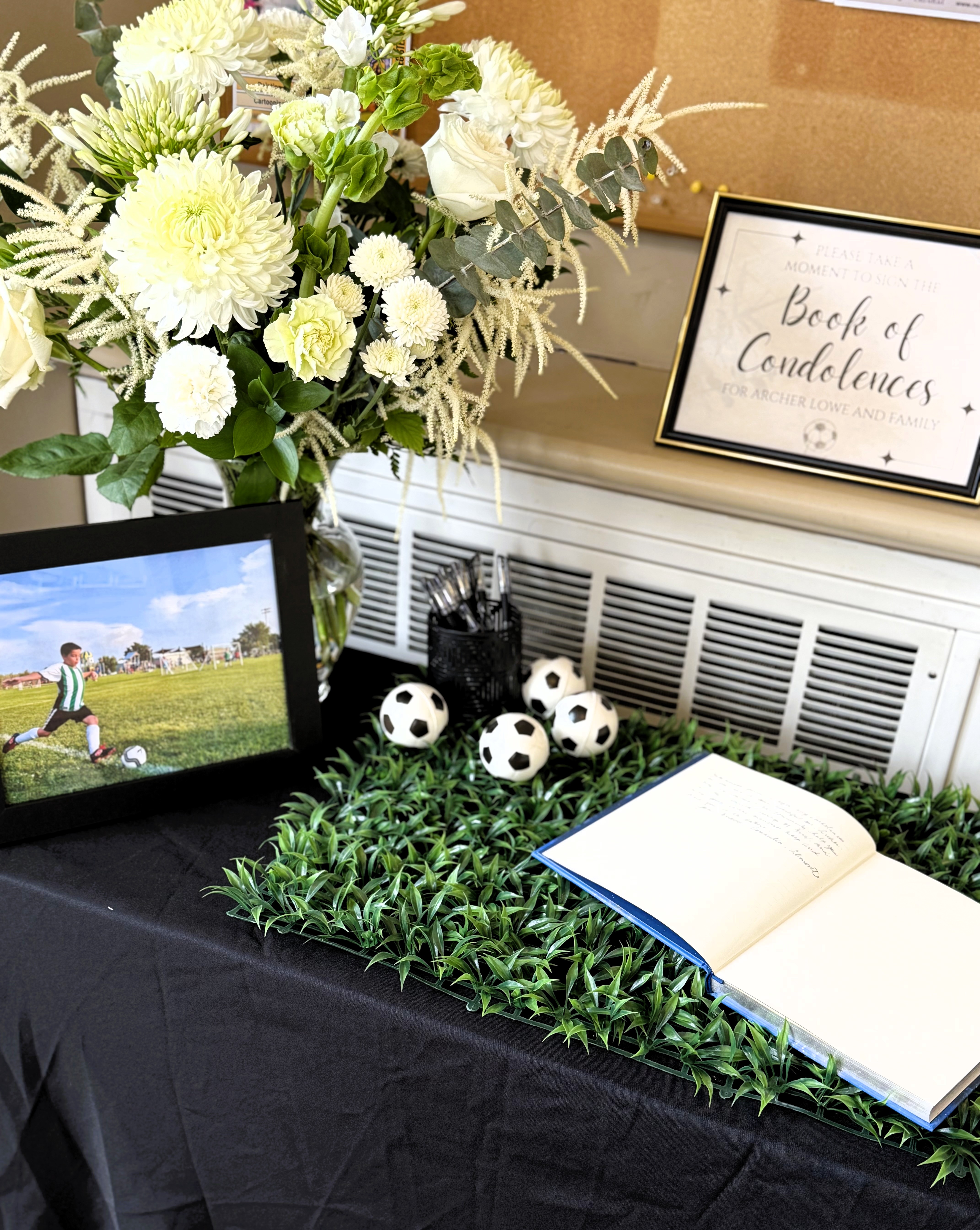 Photo of floral arrangement and a photo of a boy kicking a soccer ball. A book lays open next to the photo.