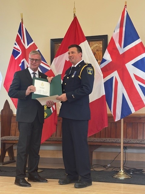 Man in uniform accepts award from man in suit